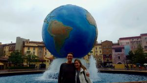 John and Heather, of Roaming Around the World, standing in front of a globe