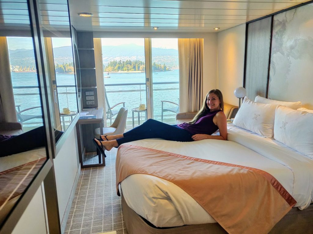 Woman lounging on bed of balcony stateroom while sailing out of Vancouver on a transpacific repositioning cruise